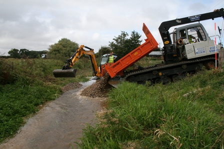 Gravel being introduced to the River Stiffkey from a tracked dumper with excavator waiting to spread them out